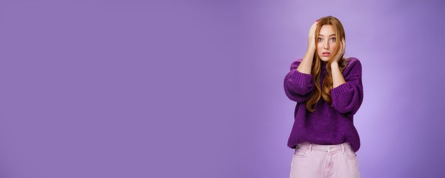 Girl in stupor feeling shocked and troubled as realising huge mistake made, holding hands on face and head popping eyes at camera confused and hopeless, posing anxious over purple background.