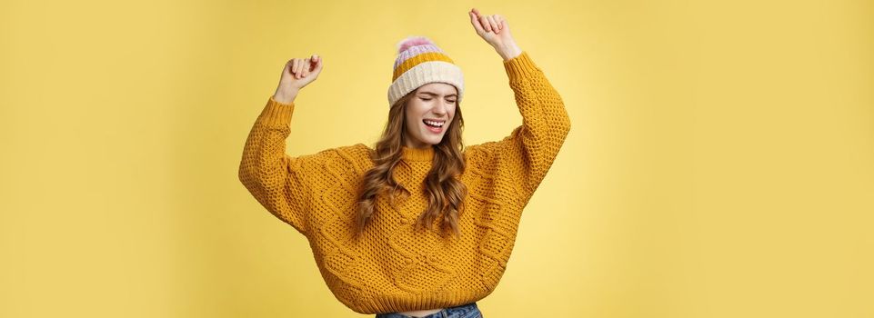 Oh yeah party vibe. Portrait joyful carefree dancing happy girl wearing winter hat sweater having fun raising hands up dancing moving music rhythm celebrating success positive news. Copy space