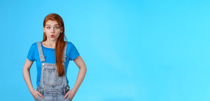 Worried nervous cute redhead female feel anxious pressured before important interview, hold breath, exhale, pouting difficult concerning situation, look insecure stand blue background.