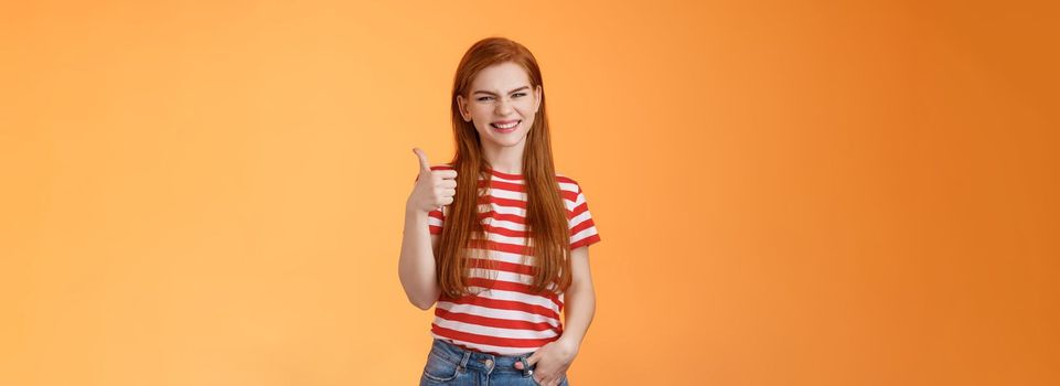Cheerful friendly woman red natural hair clean skin, show thumb up, smiling approval, support perfect choice, like excellent performance, express positive opinion, acceptance, orange background.