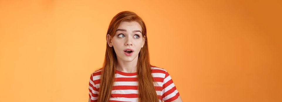 Close-up enthusiastic surprised, intrigued redhead caucasian woman look impressed left copy space, open mouth charmed amused, stare speechless, stunning cool promo, stand orange background.