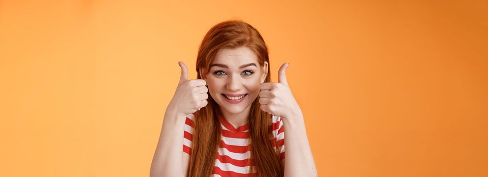 Hopeful cheerful cute redhead girlfriend rooting for you, believe win, smiling supportive satisfied, show thumbs-up delighted, approve choice, wish good luck, encourage friend, orange background.