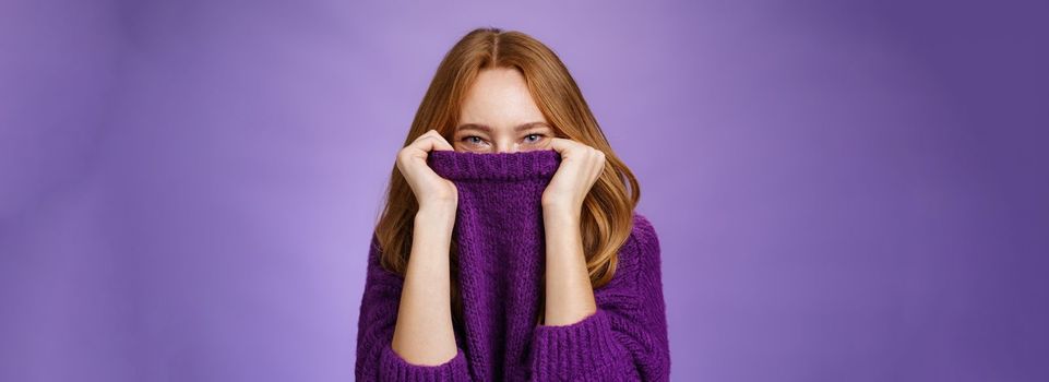 Lifestyle. Girl awaits winter with happy grin being ready warming up with cozy sweater pulling collar on face and smiling with eyes at camera standing positive and cute against purple background.