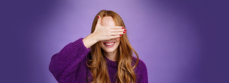 Happiness, emotions and anticipation concept. Charming dreamy ginger girlfriend with cute nails covering eyes with raised palm and smiling broadly waiting for surprise or miracle, playing peekaboo.