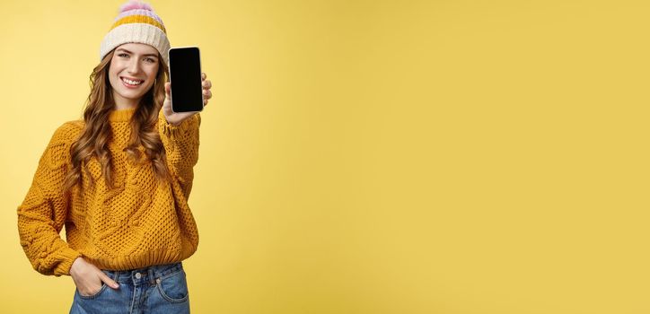 Charming outgoing smiling trendy girl extend arm showing you brand new smartphone, display grinning satisfied consulting friend what filter put using app edit photo mobile phone, yellow background.