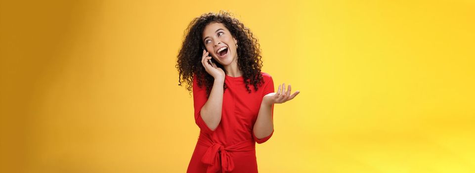 Lifestyle. Talkative glamour silly girl with curly hair having fun feeling carefree and happy taling on mobile phone turning away as laughing joyfully gesturing with hand holding smartphone pressed to ear.