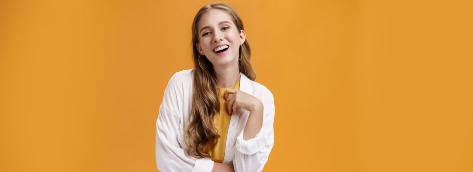 Stylish assertive and confident carefree woman dressing up on party laughing joyfully having fun and amusing talk standing pleased against orange background in white blouse over t-shirt. Fashion, lifestyle and people concept