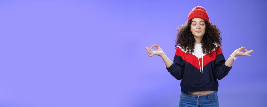 Waist-up shot of girl reaching nirvana feeling peaceful and calm holding hands sideways with mudra gesture close eyes, meditating releasing stress standing calm in lotus pose over blue background.