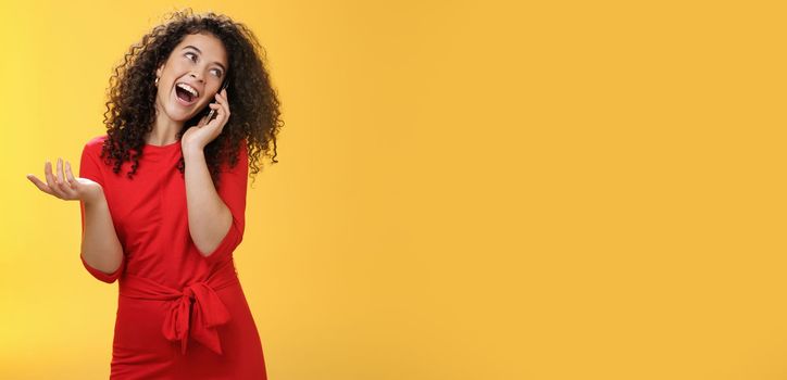 Lifestyle. Talkative glamour silly girl with curly hair having fun feeling carefree and happy taling on mobile phone turning away as laughing joyfully gesturing with hand holding smartphone pressed to ear.