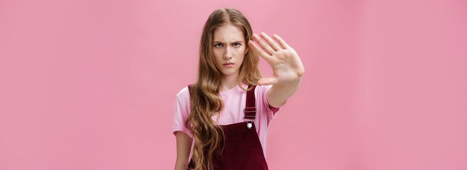 Woman protest against testing products on animals. Serious-looking confident young girl with long wavy hair frowning looking sctrict at camera pulling palm towards camera in prohibition and no gesture. Body language concept