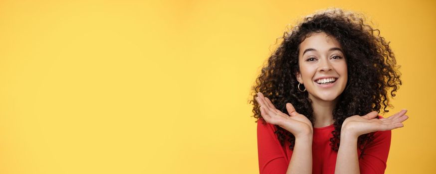 Lifestyle. Close-up shot of happy kind and tender pretty caucasian female student with curly hair and perfect skin smiling delighted holding palms spread near face having fun over yellow background.