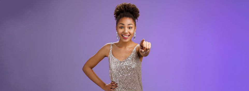 Joyful impressed african-american woman impolitely pointing camera indicating funny interesting person outfit smiling delighted staring thrilled joyful posing blue background. Copy space