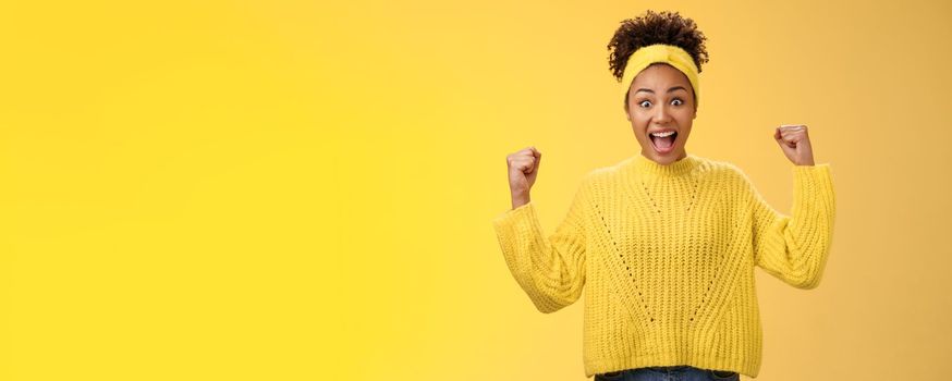 Yes finally prize mine. Excited surprised amused african-american girl celebrating victory achivement cheering smiling broadly yelling rest fists triumphing success, standing yellow background.