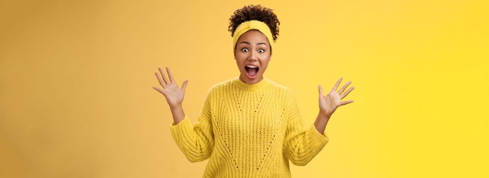 Excited happy stylish african woman in sweater yelling thrilled joyfully gesturing raised palms unbelievable luck triumphing receive extremely good perfect news, winning lottery, yellow background.