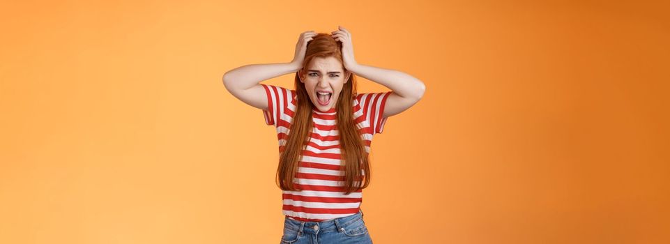 Uneasy depressed fed up pissed redhead girlfriend, scream upset, grab head, pull hair, yelling bothered, pressed, distressed, hate everyone, mental break-down, mind blowing, stand orange background.