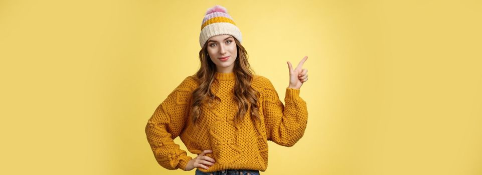 Confident good-looking young female friend telling you buy product immidietely pointing upper left corner smiling hold hand waist self-assured, employee help client pick best merch, yellow background.