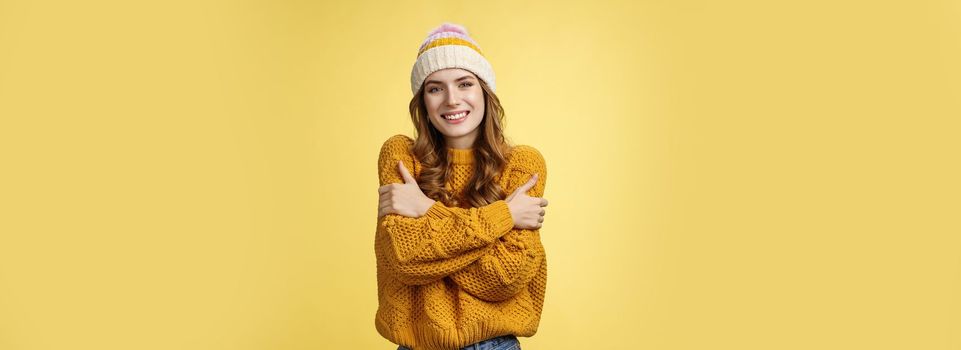 Getting cold bring jacket. Portrait charming tender feminine cute girlfriend embacing herself cuddling smiling warm gaze freezing outside standing knitted sweater hat, yellow background.