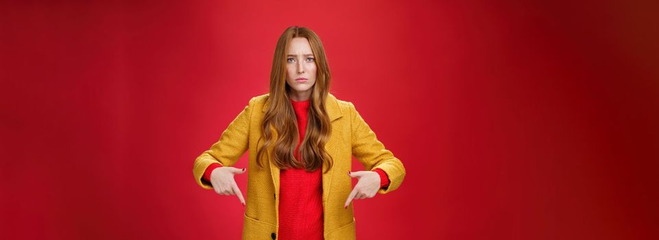 Lifestyle. Portrait of sad and displeased moody girlfriend asking opinion with concerned upset expression pointing down looking focused and serious with unhappy face at camera over red background.