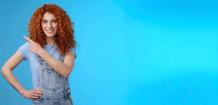 Girl suggest perfect place ad. Sassy good-looking empowered redhead daring woman smiling assertive motivated pointing upper left corner grin toothy confident you like promo blue background.