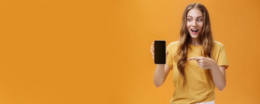 Lifestyle. Portrait of excited woman feeling amazed holding awesome new smartphone in hand pointing at cellphone screen popping eyes like crazy at device being charmed with cool technology product.