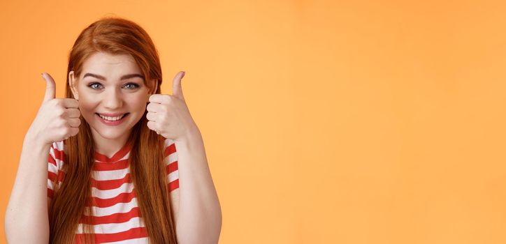 Hopeful cheerful cute redhead girlfriend rooting for you, believe win, smiling supportive satisfied, show thumbs-up delighted, approve choice, wish good luck, encourage friend, orange background.