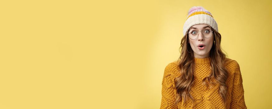 Surprised amazed charismatic good-looking young female student widen eyes wondered say wow amazed standing shocked impressed yellow background, wearing nerd glasses hat sweater.