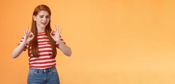 Chill carefree relaxed redhead girl assure everything fine, make okay signs, approval, nothing worry about everything good, stand orange background unbothered, satisfied not bad result.