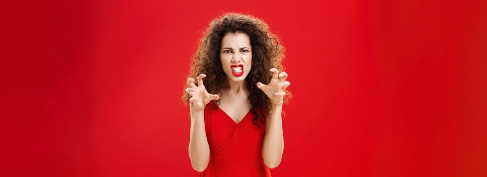 Woman like panter wanting scratch eyes of enemy. Portrait of pissed angry and pressured fed up woman clenching teeth and hands as if choking enemy with hate and anger in eyes being scary over red wall.