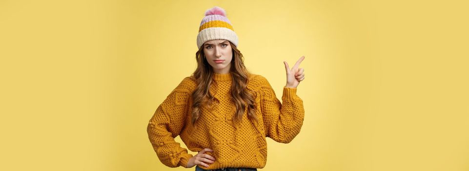 Meh lame promo. Portrait picky arrogant unimpressed complaining female fashionable customer pointing upper left corner frowning cringing displeased unsatisfied, dislike bad offer, yellow background.