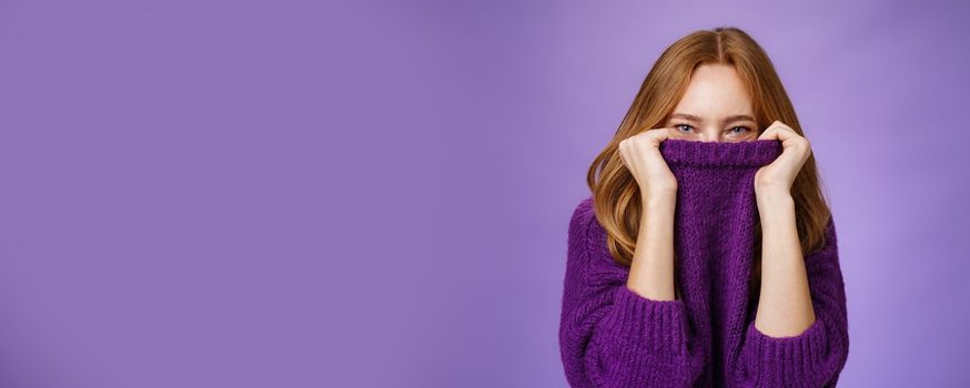 Lifestyle. Girl awaits winter with happy grin being ready warming up with cozy sweater pulling collar on face and smiling with eyes at camera standing positive and cute against purple background.