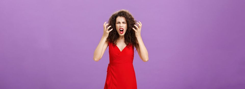 Woman getting annoyed and pissed employees spoiling her perfomance. Portrait of outraged furious female musician in red evening dress raising clenched fists grimacing and yelling angry. Copy space