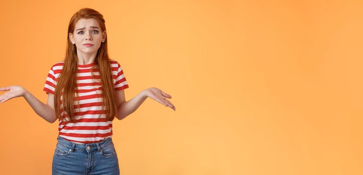 Uneasy questioned and clueless lovely modern stylish redhead woman shrugging spread hands sideways unaware, grimacing perplexed, tough question, have no answer, stand orange background.