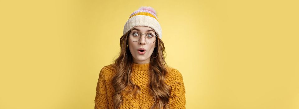 Surprised amazed charismatic good-looking young female student widen eyes wondered say wow amazed standing shocked impressed yellow background, wearing nerd glasses hat sweater.