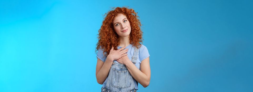 Lifestyle. Cute tender attractive redhead curly girl cherish romantic feelings thankful pleasant gift touch heart press palms chest grateful smiling broadly tilt head pleased feel loving caring emotions.