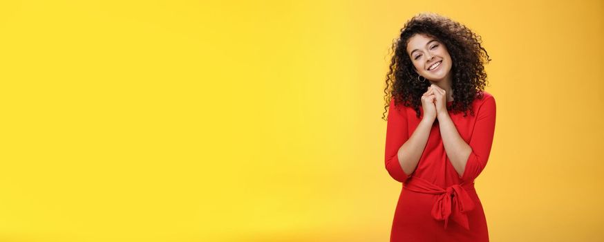 So sweet love you. Portrait of tender and silly cute curly-haired young woman in red dress tilting head holding hands together near face and smiling touched during heartwarming moment of confession.