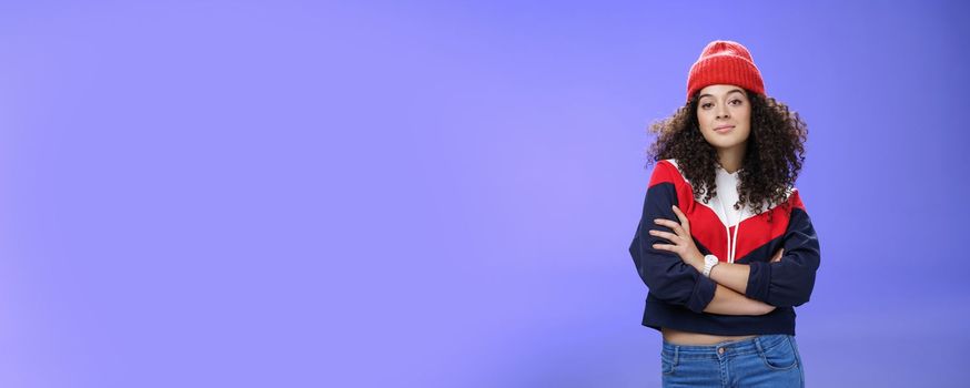 Girl will show winter who boss. Confident and stylish self-assured attractive woman with curly hair in cute red beanie and warm sweatshirt holding hands crossed over chest and looking daring at camera. Fashion, weather and people concept