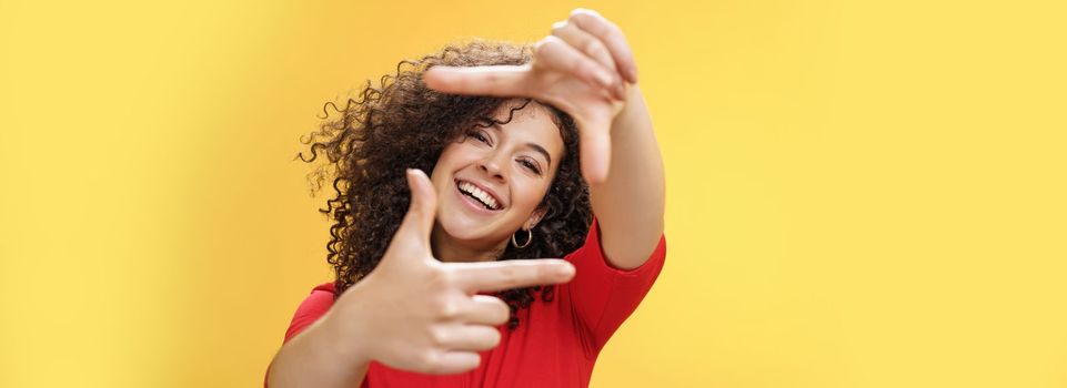 Lifestyle. Portrait of optimistic happy and creative female student imaging her new apartment as extending hands and showing frames gesture smiling through it at camera amused and carefree over yellow wall.