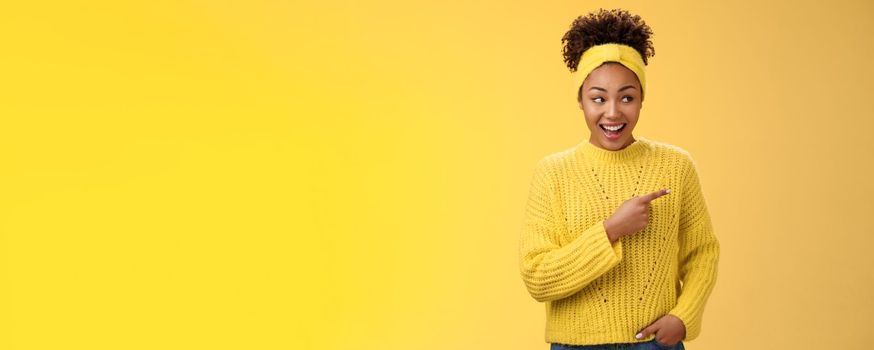 Astonished cute feminine modern african-american woman gossiping silly laughing drop jaw laughing surprised pointing right discuss during conversation interesting rumour place, yellow background.