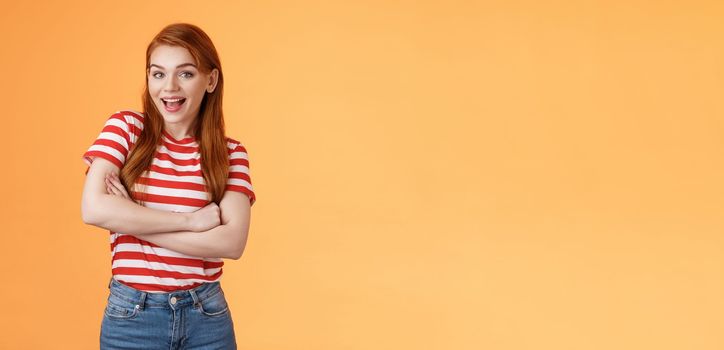 Excited cheerful ginger girl long natural red hair open mouth enthusiastic smile, cross arms chest, gladly react interesting awesome news, feel surprised pleased, stand orange background.