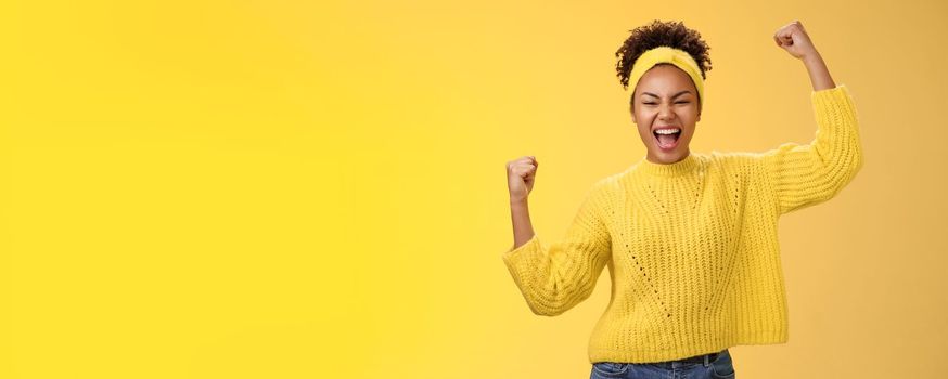 Active outgoing confident cheerful african-american female fan place bet hopefully yelling encourage team win standing raised fists victory celebrating gesture shouting proudly, yellow background.