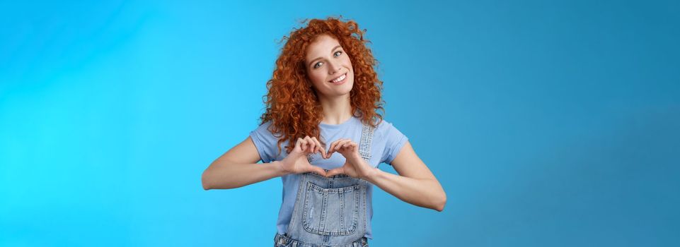 Caring tender lovely redhead girlfriend express sympathy tenderness gentle sympathy tilt head smiling broadly show heart love gesture chest cherish passionate romantic feelings, blue background.