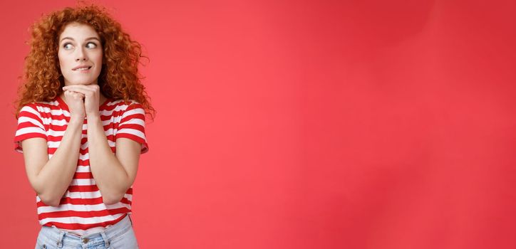 Cheerful intrigued redhead silly curly-haired woman smiling interested hold hands chin face-line imaging thinking about tasty burger look away desire have bite standing red background. Copy space