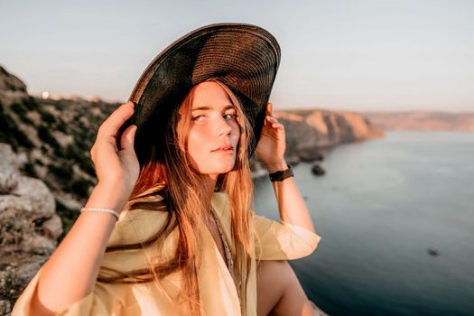 Portrait of happy young woman wearing summer black hat with large brim at beach on sunset. Closeup face of attractive girl with black straw hat. Happy young woman smiling and looking at camera at sea