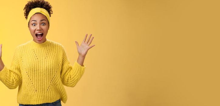 Excited happy stylish african woman in sweater yelling thrilled joyfully gesturing raised palms unbelievable luck triumphing receive extremely good perfect news, winning lottery, yellow background.