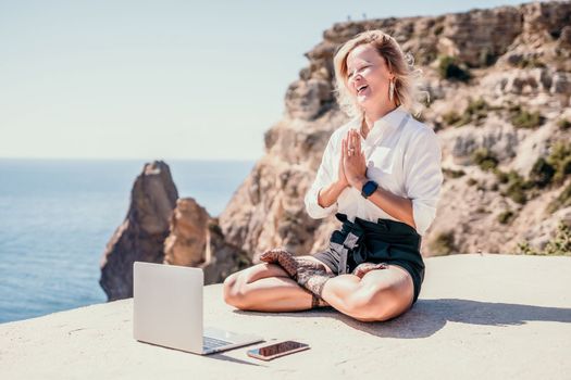 Happy girl doing yoga with laptop working at the beach. beautiful and calm business woman sitting with a laptop in a summer cafe in the lotus position meditating and relaxing. freelance girl remote work beach paradise