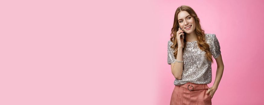 Good-looking sociable european curly-haired woman wearing glitter blouse calling friend discuss party smiling broadly feeling carefree happy, holding smartphone waiting pick up phone.