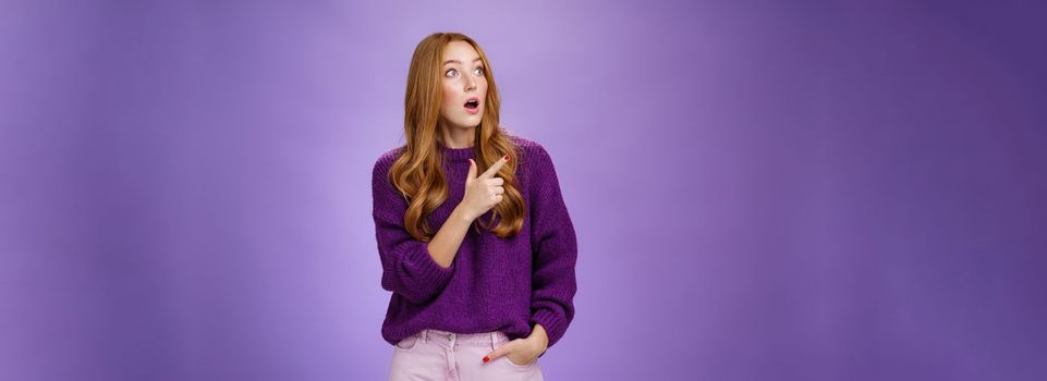 Girl surprised and thrilled as seing unbelievable scene. Portrait of impressed and shocked good-looking ginger woman in purple sweater gasping from amazement pointing, looking left intrigued.