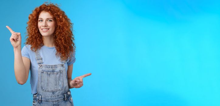 Lifestyle. Lively joyful good-looking 25s redhead curly-haired sassy girl summer positive mood dancing overalls pointing sideways up right index fingers directing promos store links smiling delighted.