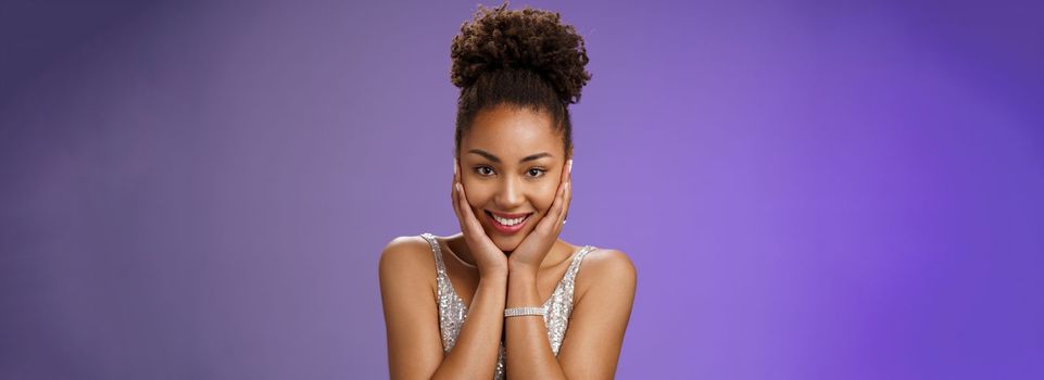 Close-up amused tender romantic african-american woman. in stylish glittering silver evening dress touch cheeks blushing cute glad receive passionate compliments standing amused blue background.