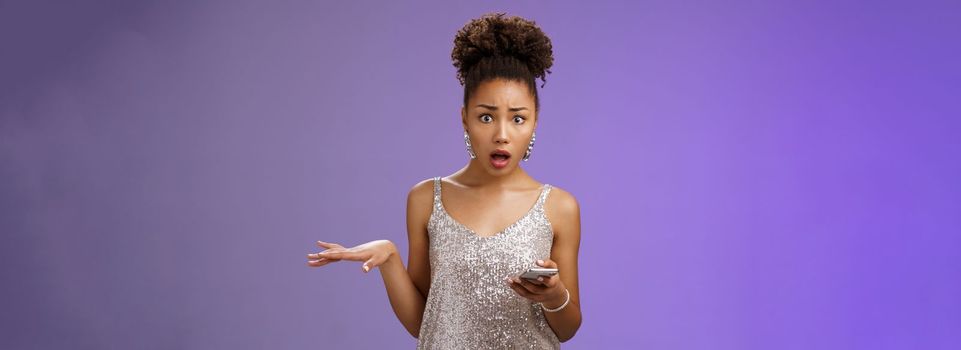 Concerned troubled arrogant silly glamour african american woman raise hand questioned holding smartphone insulted during phone call standing frustrated upset bothered blue background.